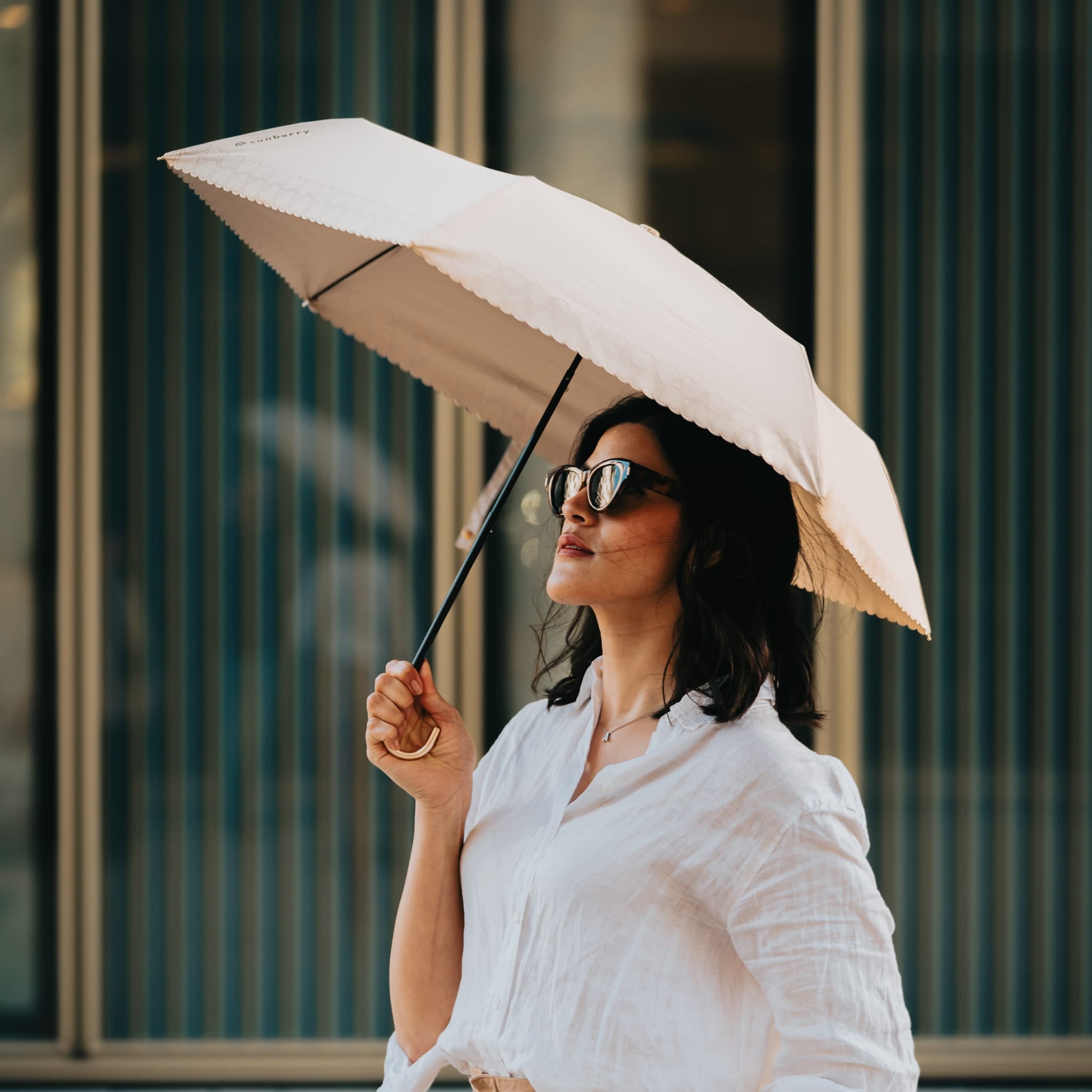 Frau mit Sunbarry Romantic Breezer Pearl Beige in der Stadt – UV-Schirm mit Herzbordüre und Goldgriff#Color_Pearl Beige